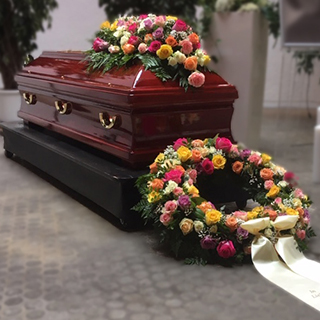 Sarg mit buntem Blumengesteck und Trauerkranz